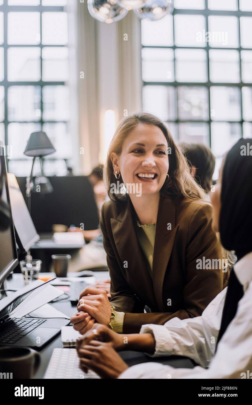 Eine glückliche Geschäftsfrau mittleren Erwachsenen, die mit einer Kollegin am Schreibtisch im Büro spricht Stockfoto