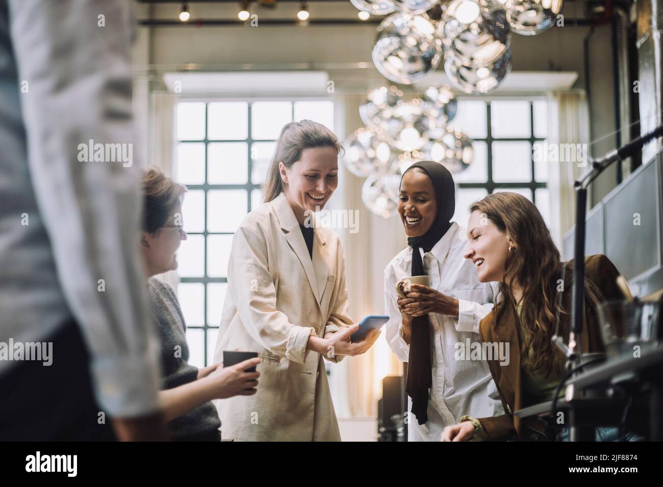Glückliche Geschäftsfrau mit mittlerem Erwachsenenalter, die im Büro ein Smartphone mit einem Kollegen und einer Kollegin teilt Stockfoto