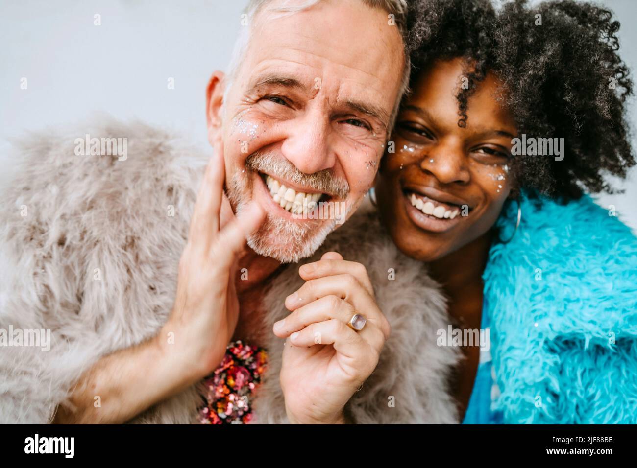 Porträt einer lächelnden Frau und eines schwulen Mannes mit glänzendem Blusher auf den Gesichtern zu Hause Stockfoto