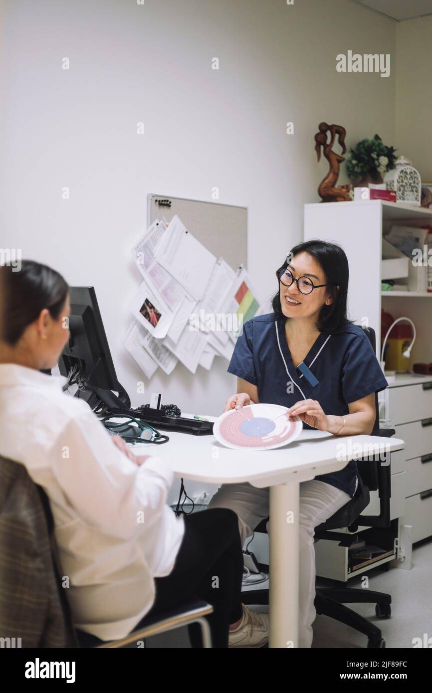 Lächelnde Ärztin zeigt in-vitro-Befruchtungskarte, während sie mit dem Patienten im Krankenhaus spricht Stockfoto