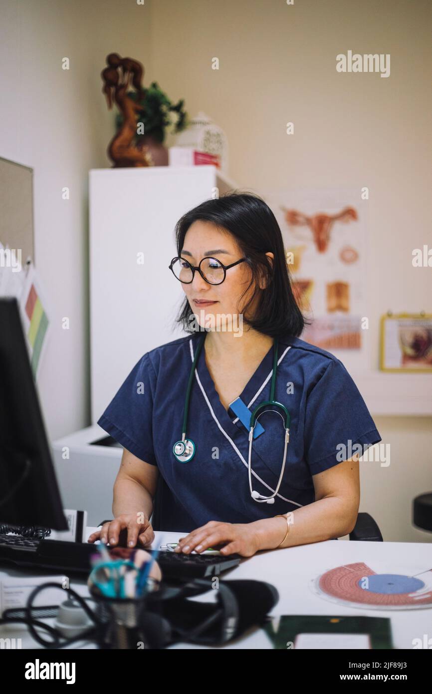 Lächelnde Expertin im Gesundheitswesen, die Computer am Schreibtisch im Büro benutzt Stockfoto