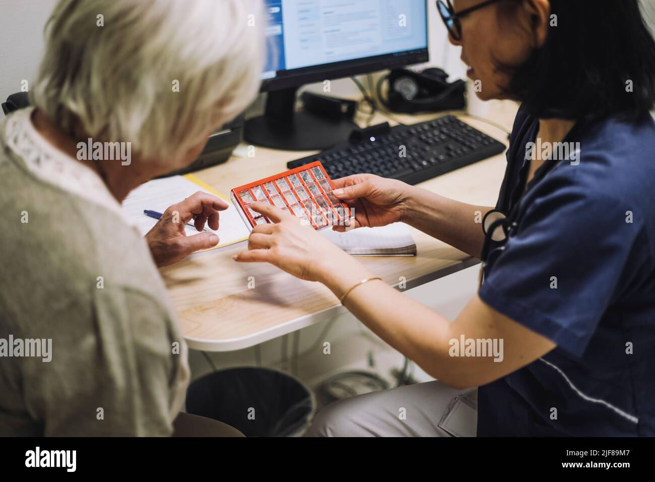 Ärztin diskutiert über den Pillenorganisator mit einer älteren Patientin, die am Schreibtisch im Büro sitzt Stockfoto