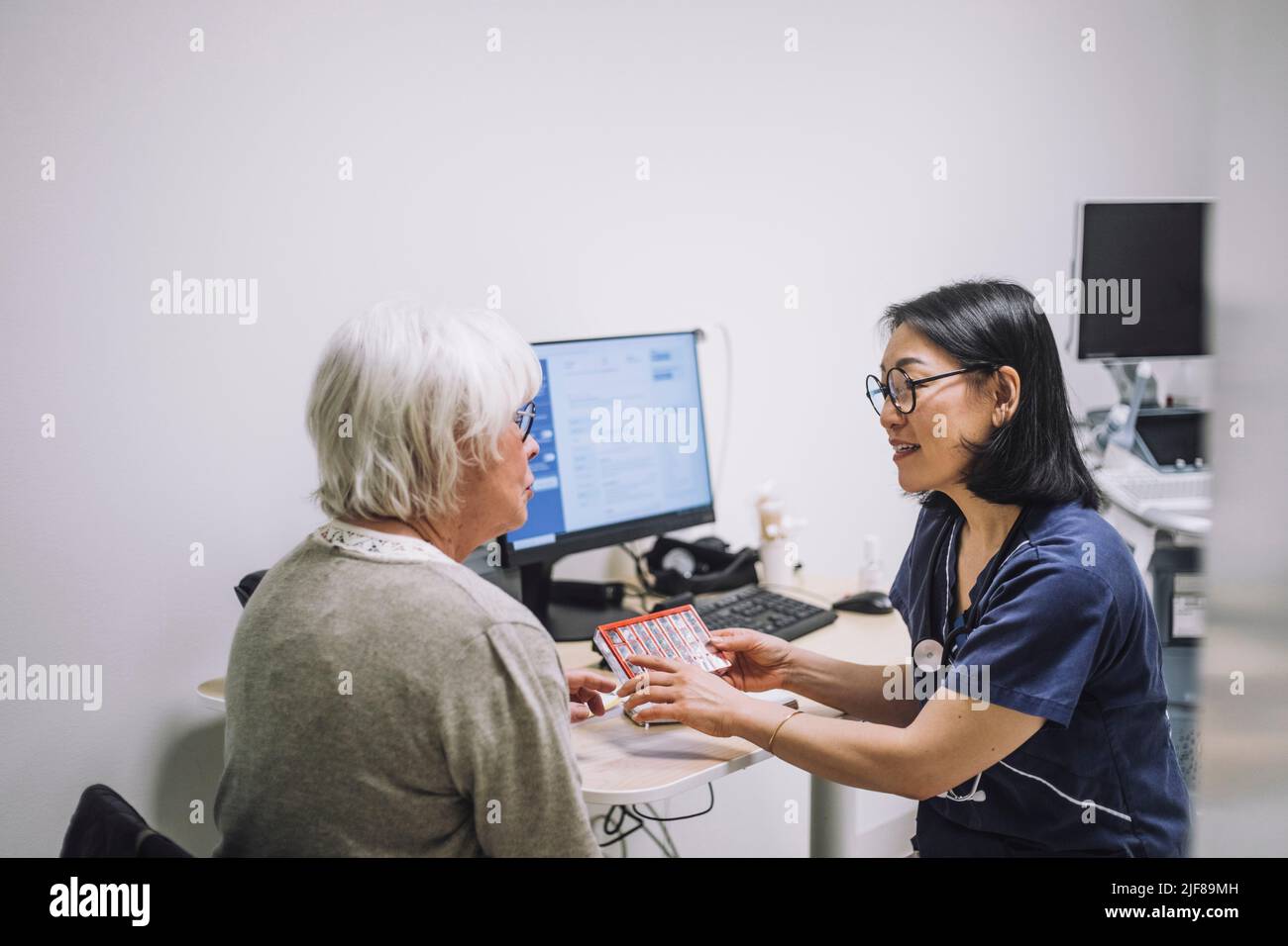 Reife Ärztin diskutiert über Pille Organisator mit älteren Patienten im Krankenhaus Stockfoto