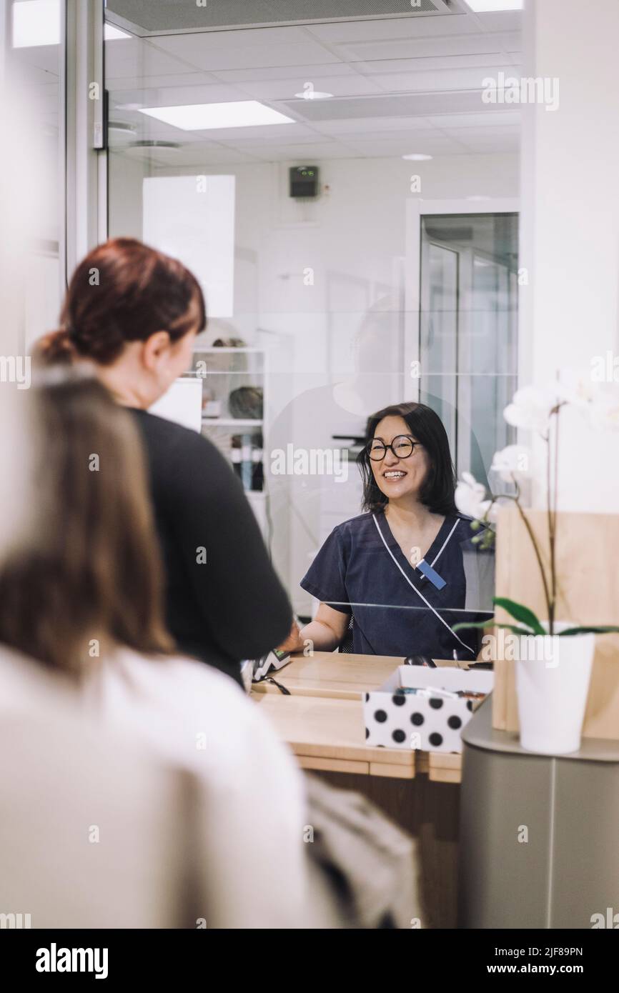 Lächelnde Dame an der Rezeption, die dem Patienten beim Auschecken in der medizinischen Klinik hilft Stockfoto