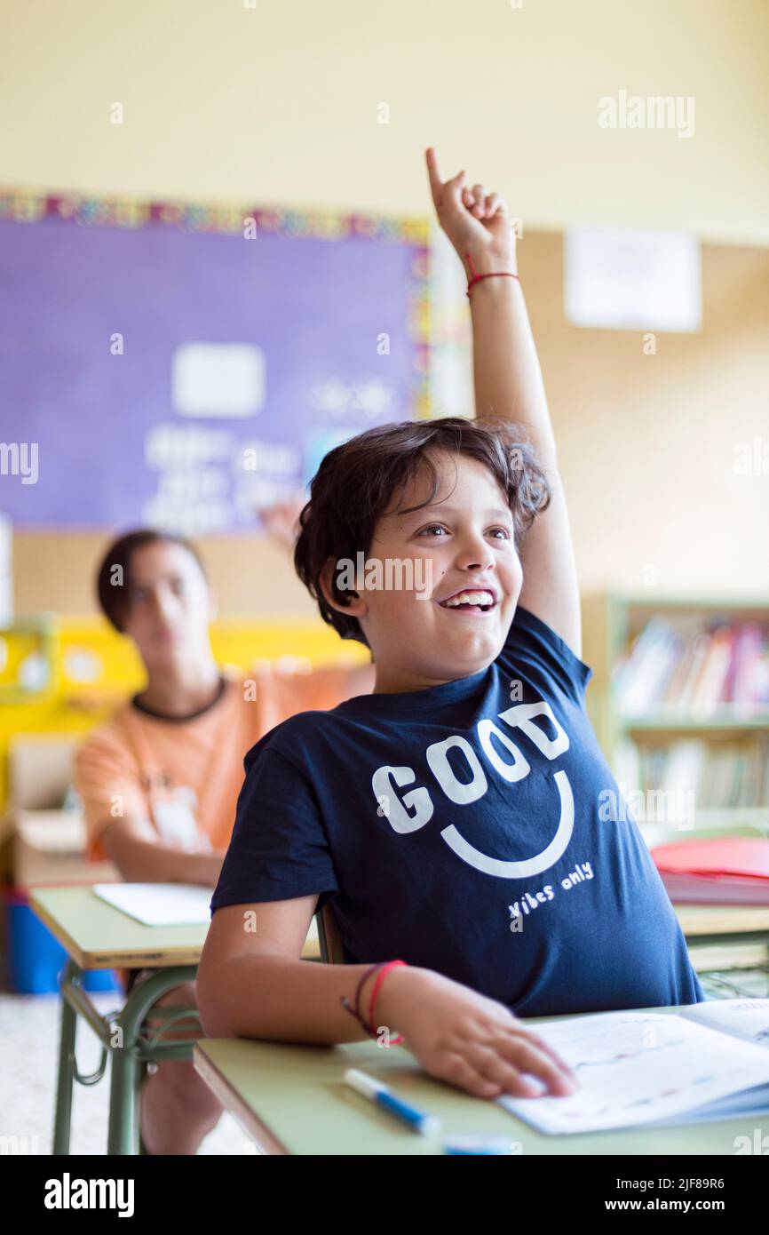 Porträt eines lächelnden kaukasischen Kindes mit erhobener Hand im Unterricht. Grundschulbildung. Zurück zur Schule. Stockfoto