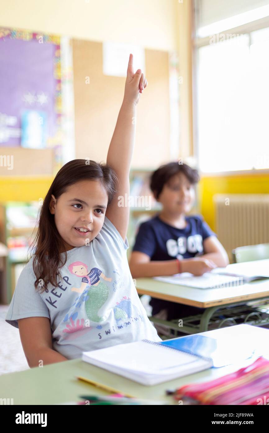 Porträt eines kleinen kaukasischen Mädchens mit erhobener Hand in der Klasse. Grundschulbildung. Zurück zur Schule. Stockfoto