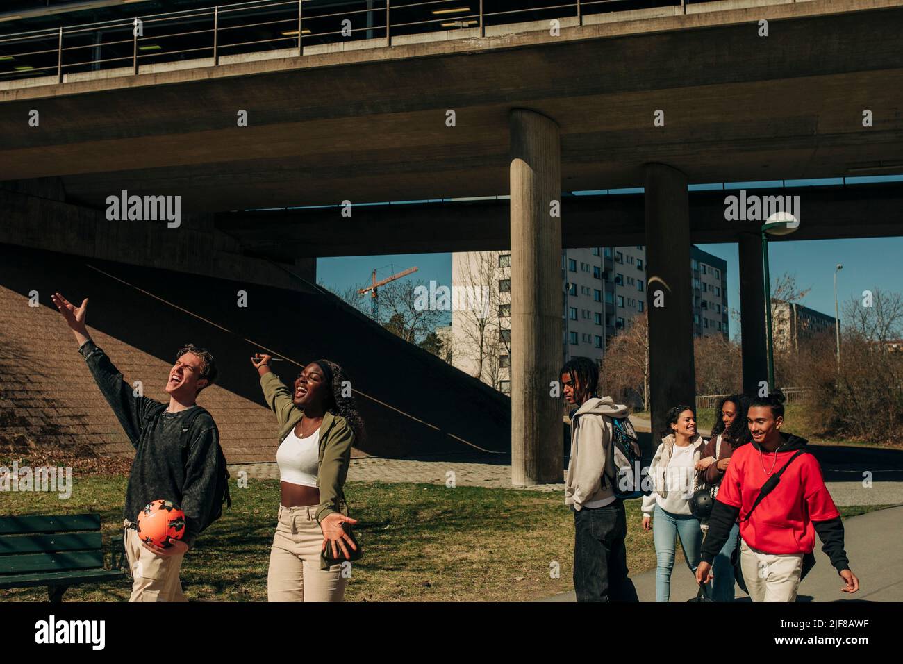 Multirassischer junger Mann und Frau singen, während Freunde an einem sonnigen Tag in der Stadt spazieren Stockfoto