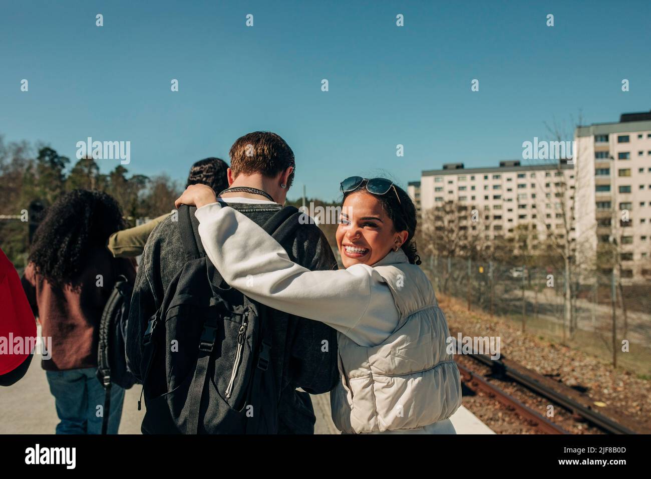 Glückliche Frau, die an einem sonnigen Tag mit dem Arm um einen Freund über die Schulter schaut Stockfoto