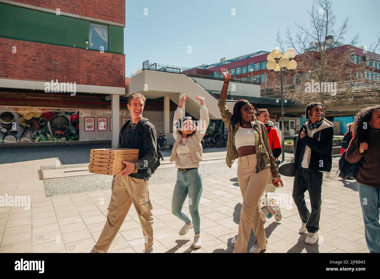 Glückliche multirassische Freunde winken die Hände, während sie an einem sonnigen Tag auf der Straße spazieren Stockfoto
