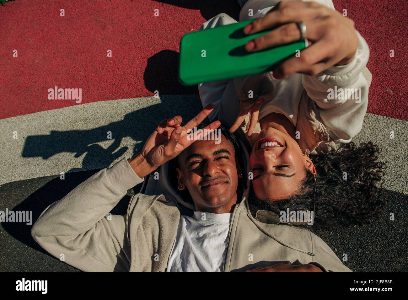 Freunde, die ein Friedenszeichen bilden, während sie Selfie über das Smartphone machen, das auf dem Spielplatz liegt Stockfoto