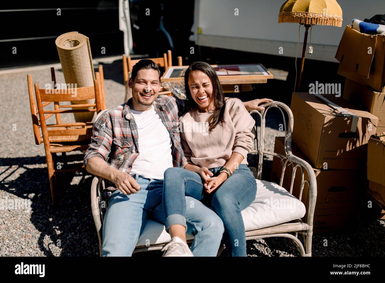 Porträt eines lächelnden Paares, das während eines sonnigen Tages auf einem Stuhl sitzt Stockfoto