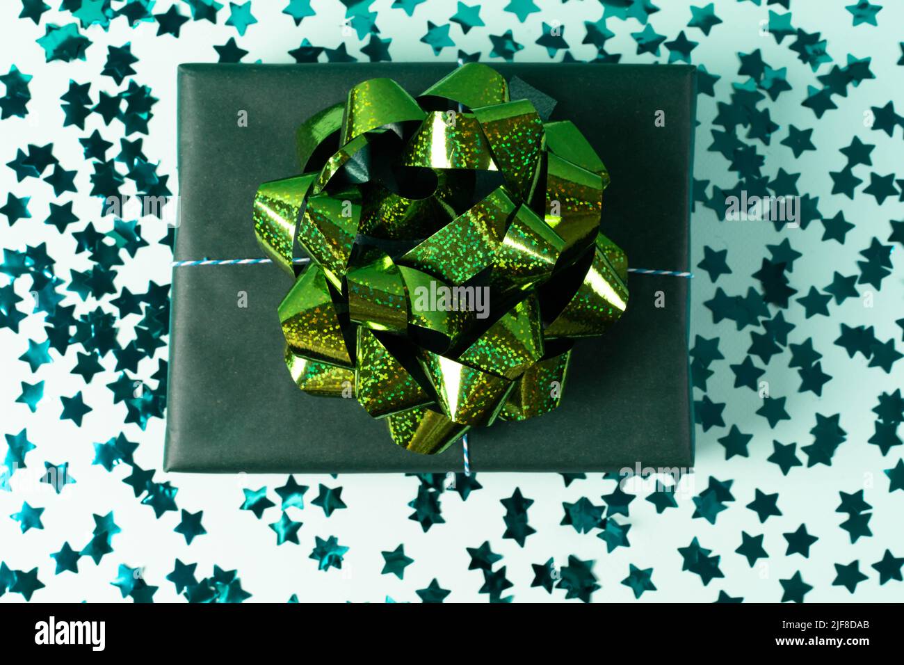 Grüne Geschenkbox aus Kraftpapier mit Schleife auf blauem Hintergrund mit Konfetti. Weihnachtsgeschenk, valentinsüberraschung, Geburtstagskonzept. Flach liegend Stockfoto