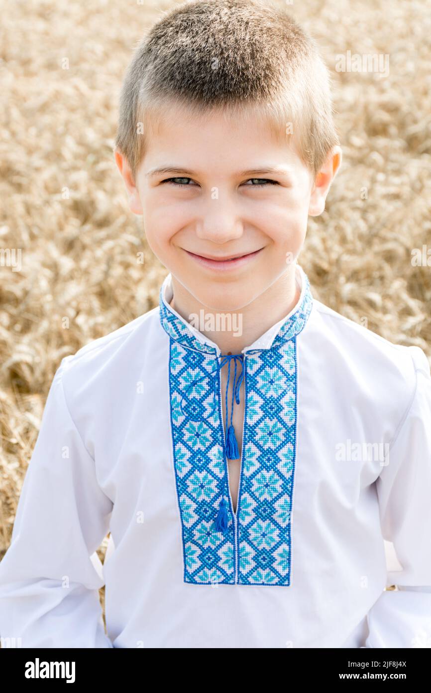 Porträt des Kindes in traditionellen bestickten ukrainischen Hemd auf dem Hintergrund des Weizenfeldes an sonnigen Tag. Blaue Stickerei. Junge lächelt aufrichtig. Unabhängigkeitstag, Verfassung der Ukraine. Vertikal Stockfoto