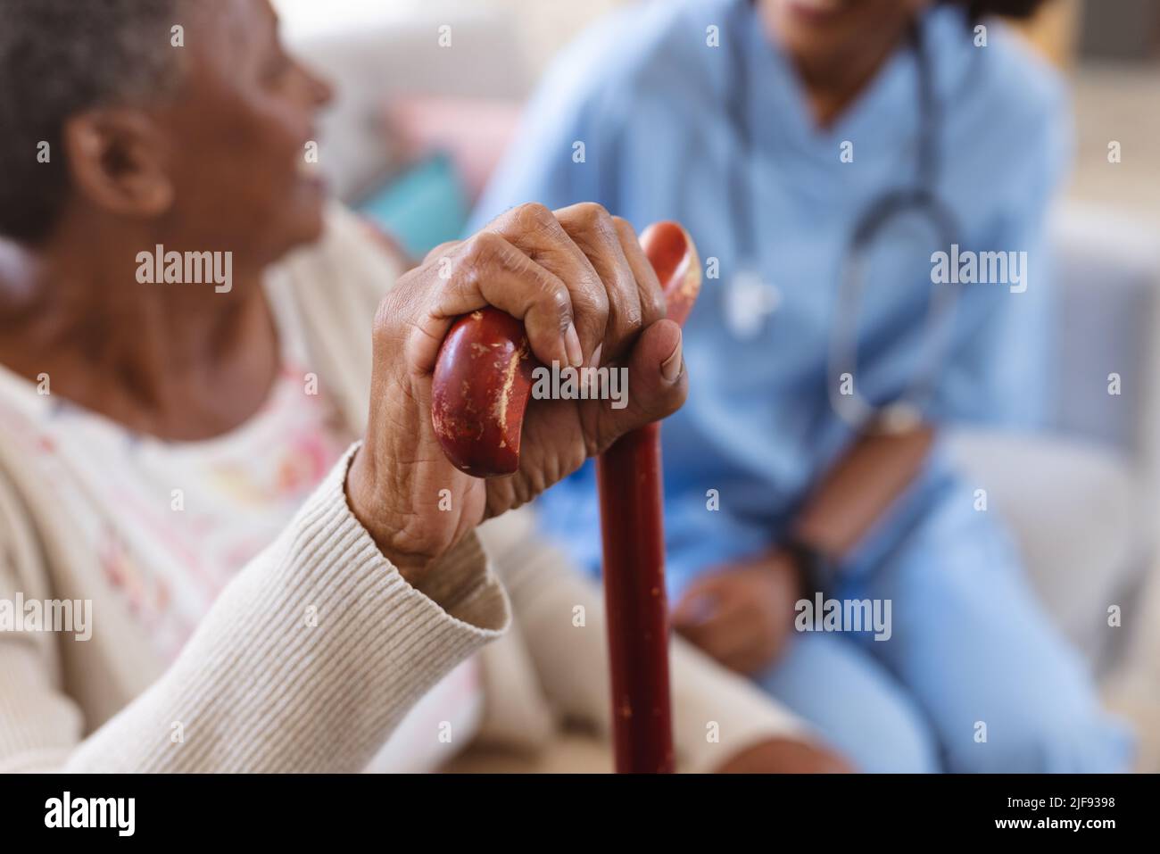 afroamerikanische ältere Frau mit Gehstock, die zu Hause mit einer Ärztin auf dem Sofa sitzt Stockfoto