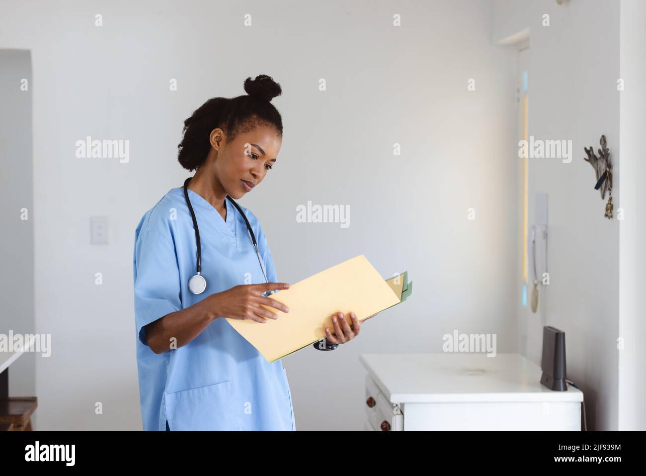 afroamerikanischer junger Arzt mit Stethoskop um den Hals, der medizinische Berichte gegen die Wand liest Stockfoto