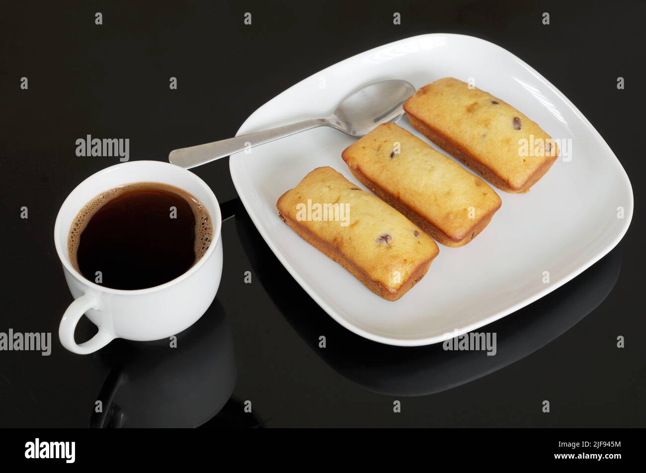 Tasse Kaffee und Kuchen mit Schokoladenstückchen auf schwarzem Tisch Stockfoto