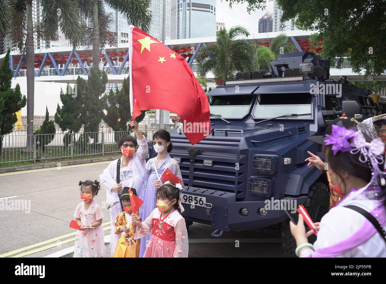 Menschen in einer feierlichen Prozession posieren mit einer chinesischen Flagge in der Nähe eines gepanzerten Fahrzeugs der Polizei. Xi Jinping, der chinesische Führer, ist heute in der SAR-Stadt, um an der Zeremonie zum Übergabejubiläum 25. teilzunehmen, sowie an der Vereidigung des neuen Chefs von Hong Kongs, John Lee. Stockfoto