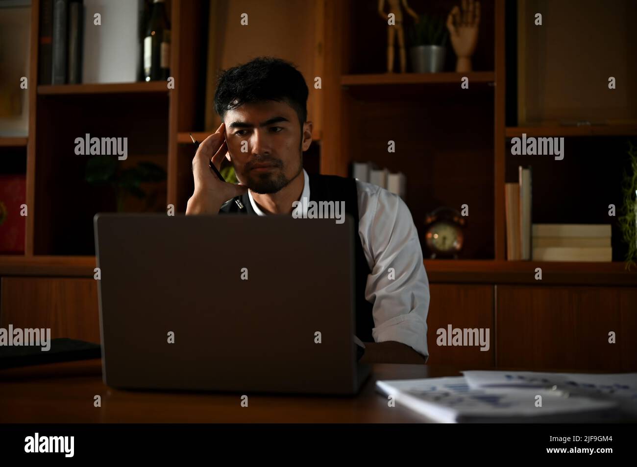 Seriöser asiatischer Geschäftsmann oder leitender Manager, der am Laptop-Computer arbeitet und an seinem Schreibtisch nach Plänen für Geschäftslösungen sucht Stockfoto