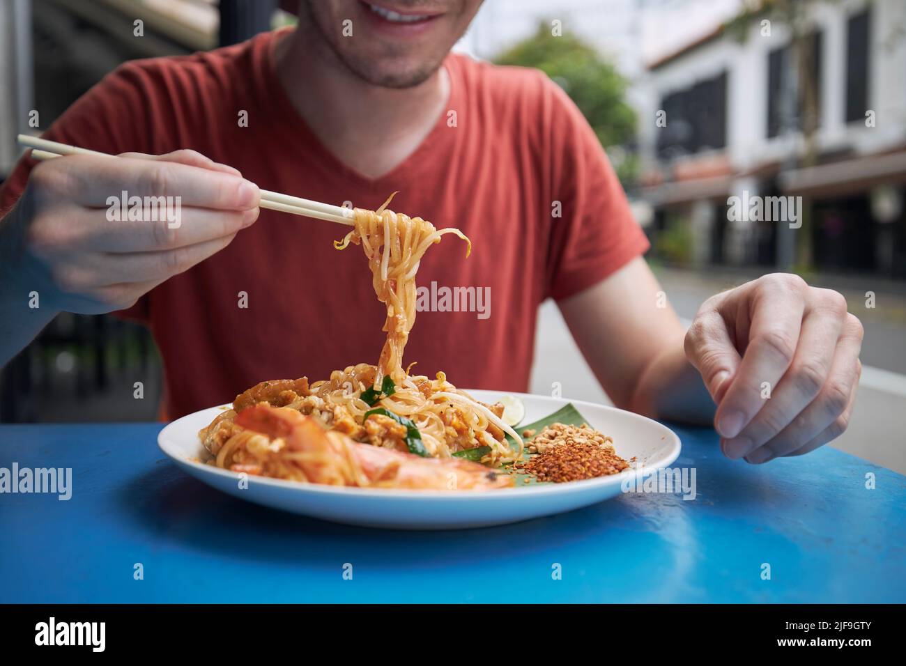 Nahaufnahme von Essstäbchen mit Pad Thai Food. Mann, der in Singapur im Straßenrestaurant am Straßenrand isst. Stockfoto