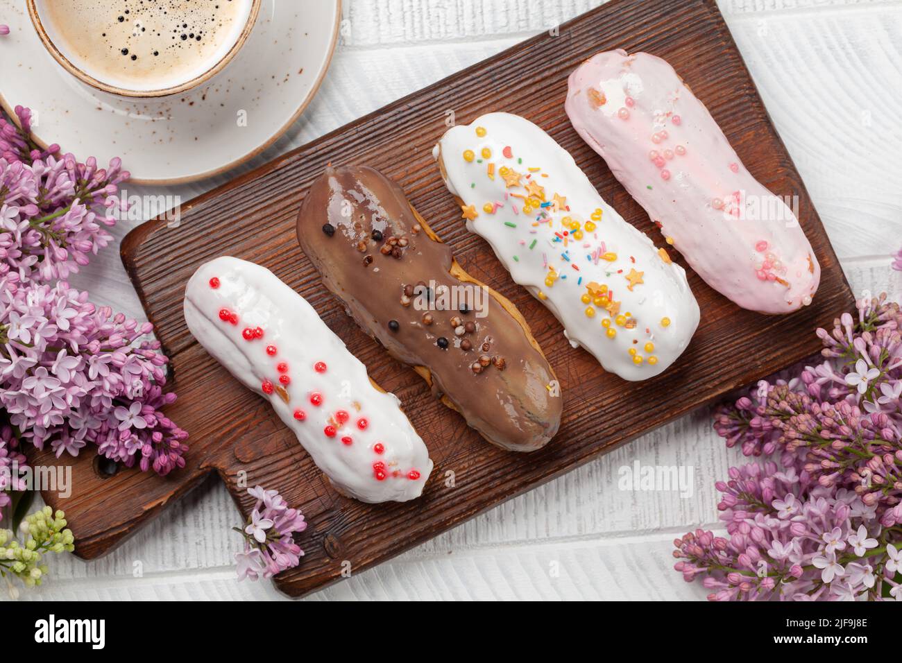 Eclair Dessert und Kaffee. Auf Holztisch mit Fliederblumen. Draufsicht flach liegend Stockfoto