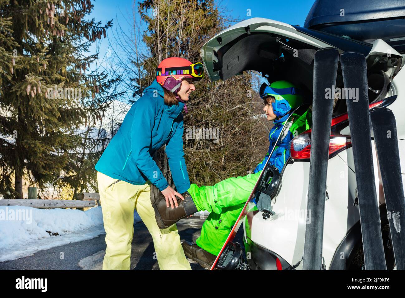 Mutter helfen Sohn auf Snowboard Stiefel sitzen im Kofferraum zu setzen Stockfoto