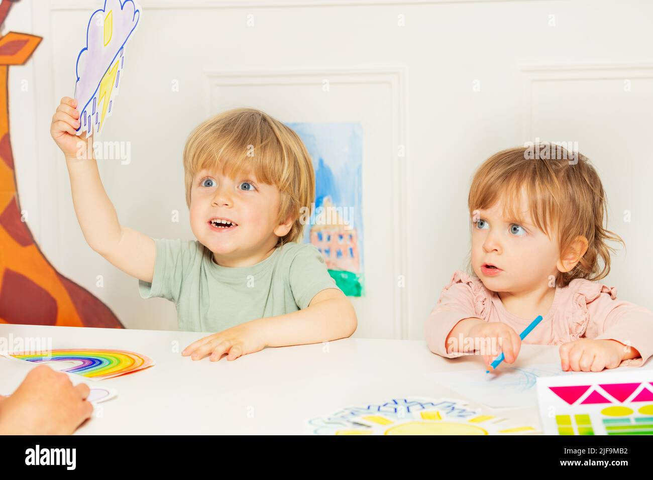 Junge und ein Mädchen zeigen Wetterkarten, die in der Kindergartenklasse sitzen Stockfoto