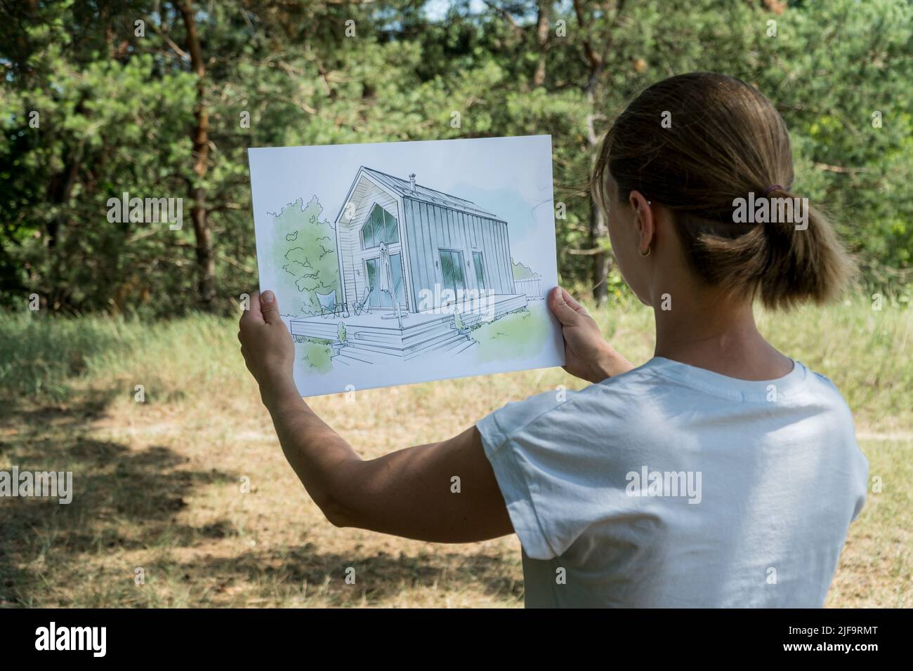 Architekt hält Scheunenhaus handgezeichnete Skizze vor einem Grundstück. Architektonisches Designkonzept Stockfoto