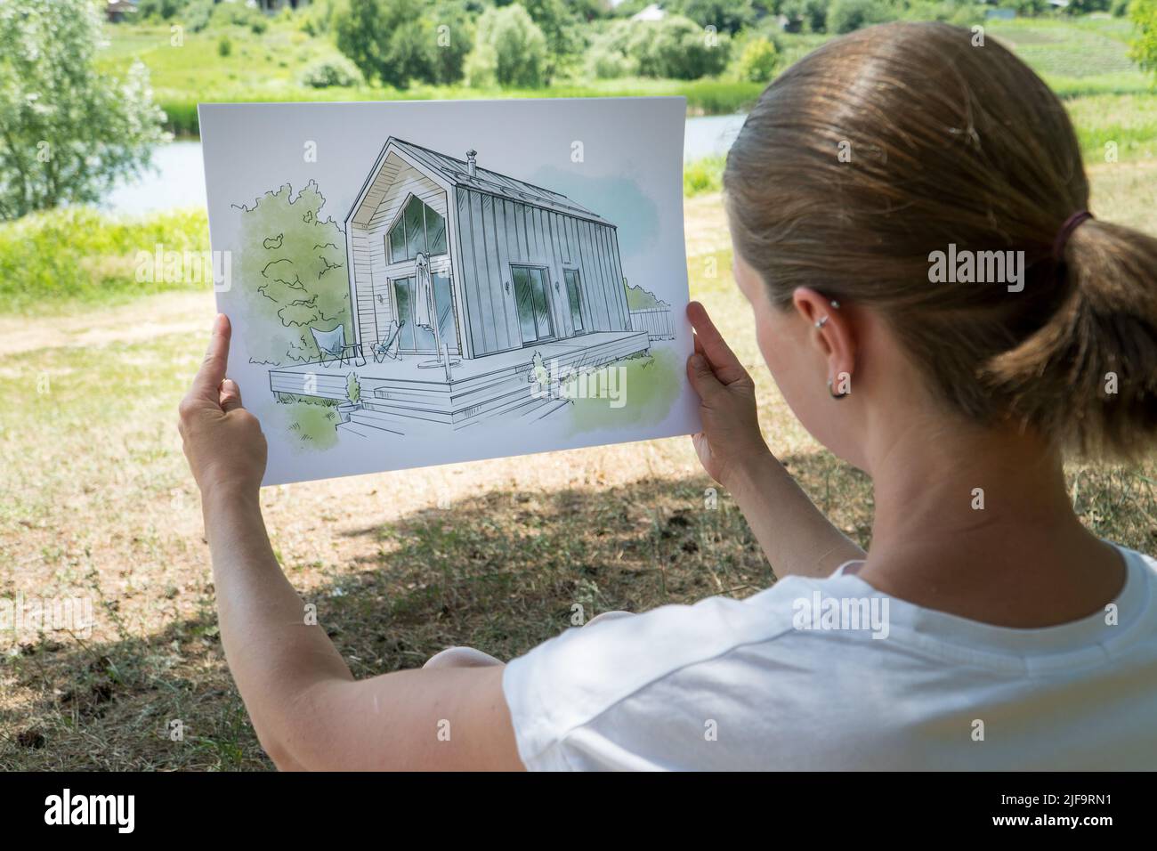 Architekt hält Scheunenhaus handgezeichnete Skizze vor einem Grundstück. Architektonisches Designkonzept Stockfoto