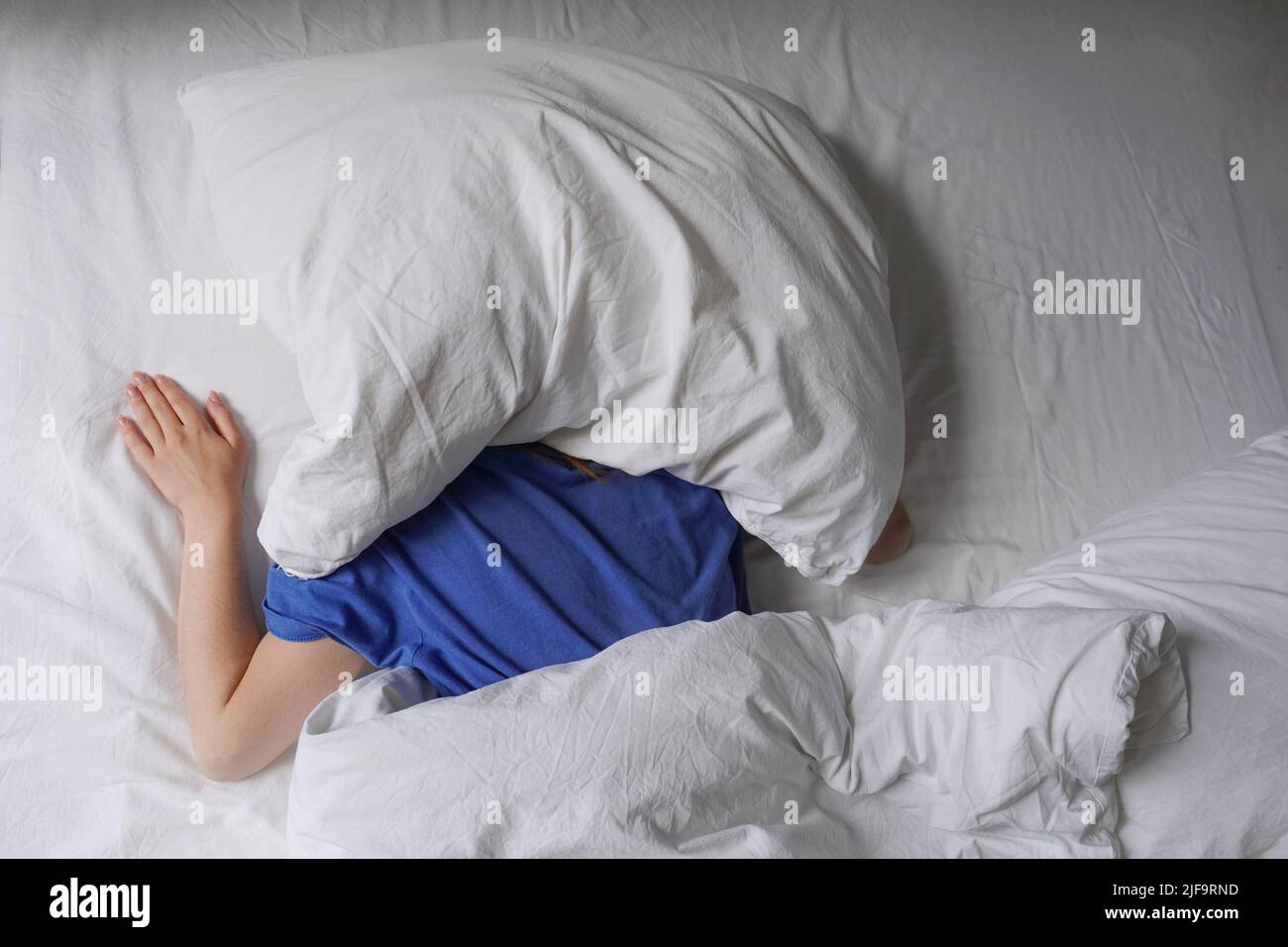 Frau, die im Bett schlief, mit Kissen über dem Kopf Stockfoto