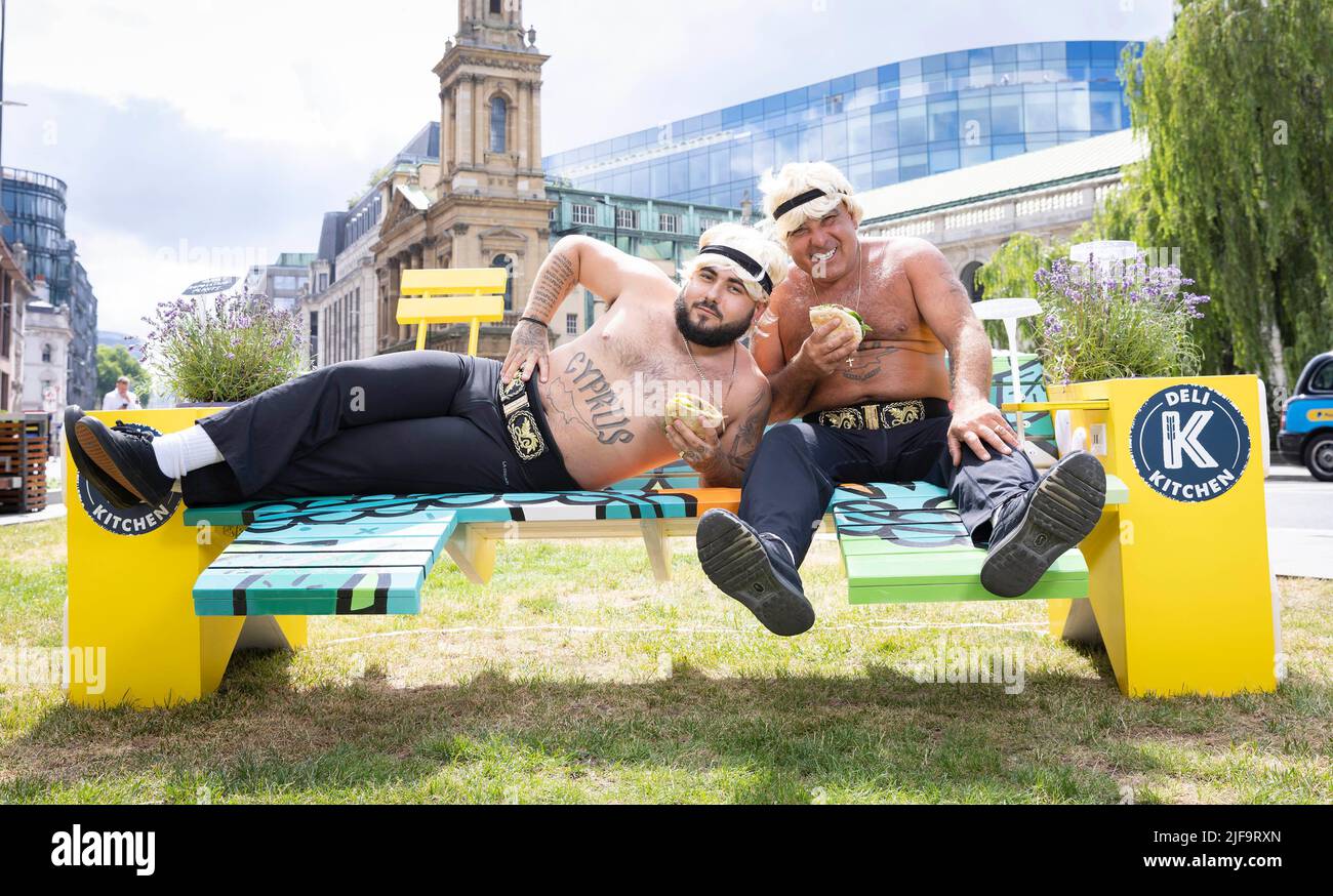 NUR FÜR REDAKTIONELLE VERWENDUNG das Tanzduo Stavros Flatley sitzt auf einer speziell gestalteten Eat Wild Parkbank im Holborn Circus in London, die von Deli Kitchen entwickelt wurde, um britische Arbeiter zu Mittagspausen im Freien zu ermutigen. Bilddatum: Freitag, 1. Juli 2022. Stockfoto