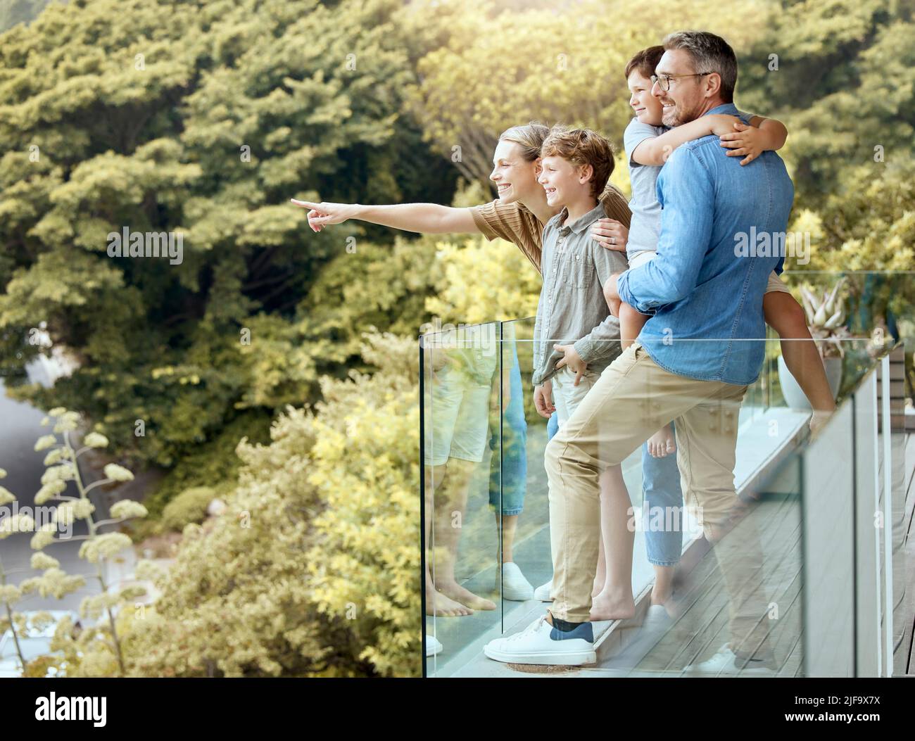 Eine fröhliche vierköpfige kaukasische Familie, die die Aussicht von einem Balkon zu Hause genießt. Lächelndes Paar, das sich mit ihren Söhnen im Urlaub verbindet Stockfoto