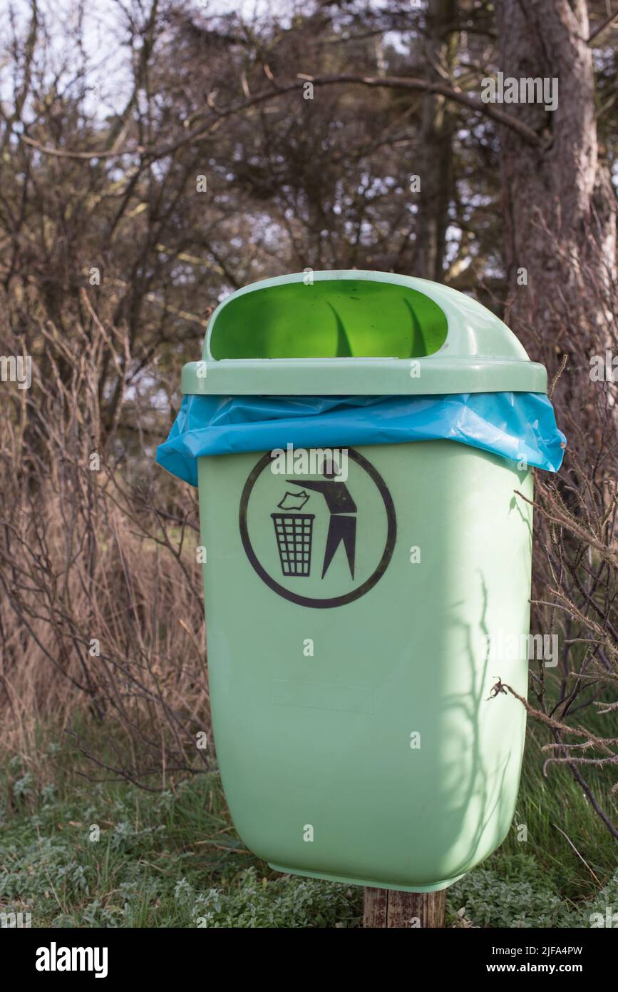 Leeren Sie den hellgrünen Mülleimer oder Mülleimer mit einem blauen Müllbeutel und einem Piktogramm im Winter in einem Wald oder Park mit Bäumen im Hintergrund Stockfoto