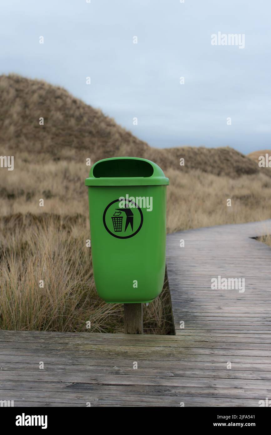 Hellgrüner Abfalleimer mit Piktogramm in den Sanddünen von Amrum (Deutschland) an einem Nachmittag im Winter neben einer Promenade Stockfoto