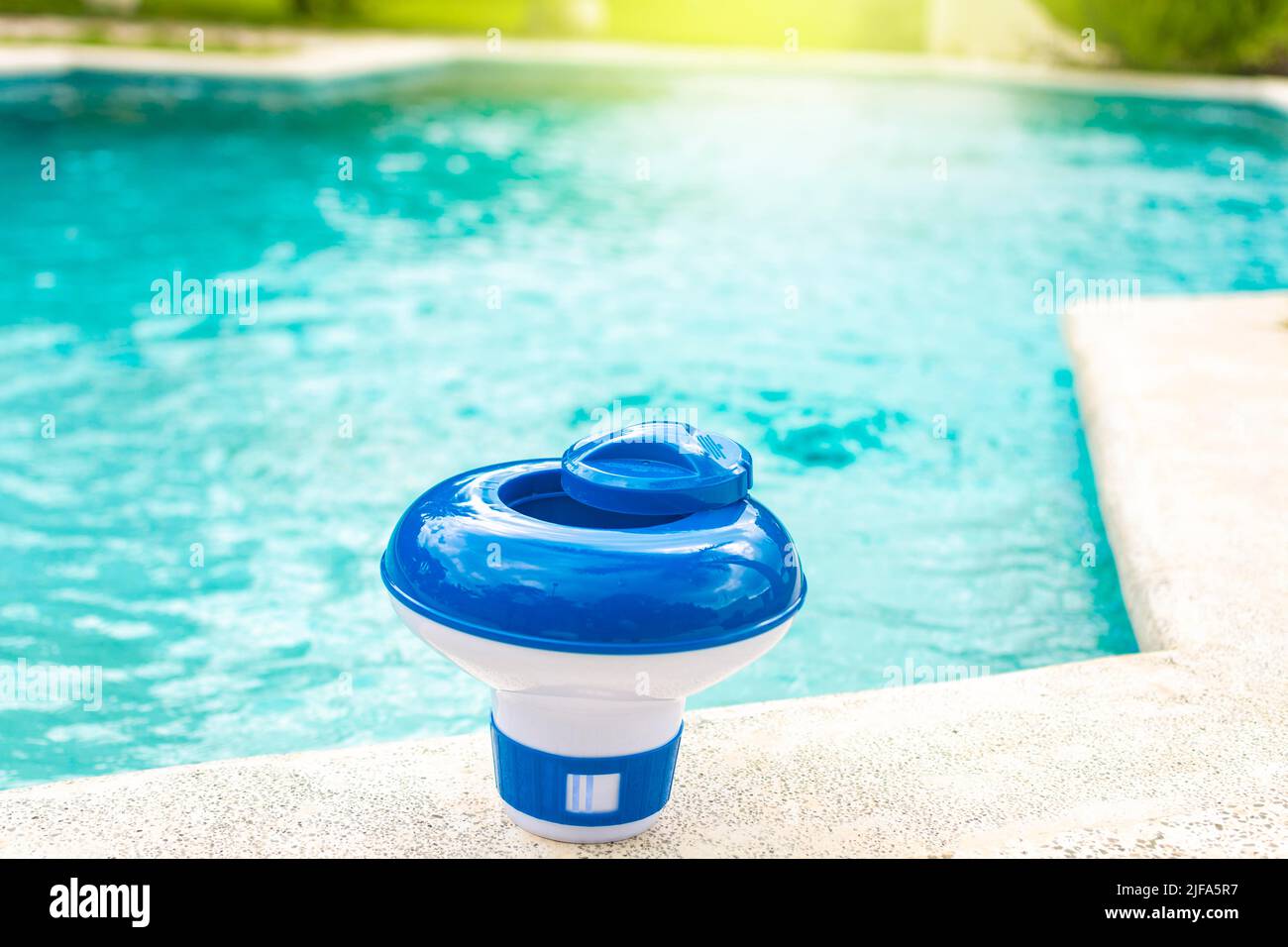 Ein Chlorspender für Schwimmbäder mit blauem Wasser im Hintergrund. Dosierschwimmbad zur Chlorierung von Schwimmbädern, Ein Chlorschwimmbad am Rand Stockfoto