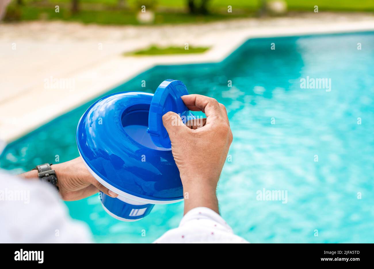 Hände eines Arbeiters, der einen Schwimmer für Chlor in einem Pool installiert, eine Person, die einen Spender für Chlor in einem Pool hält. Hände mit einem Chlorspender für den Pool. Hand eines Stockfoto