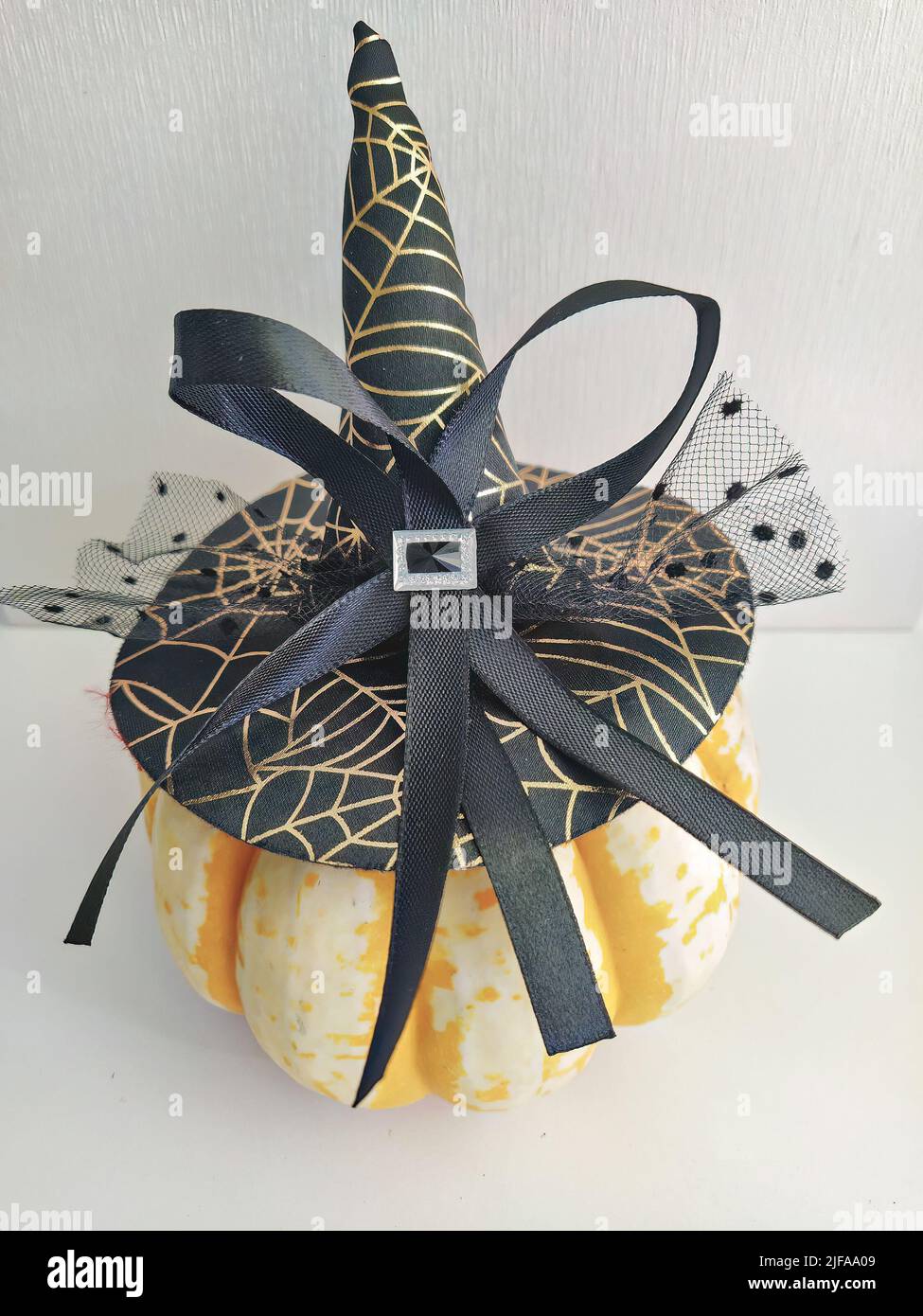 Natürlich reifer Kürbis mit einem eleganten Hexenhut mit Schleife und Schleier verziert. Halloween Hausdekoration Konzept Stockfoto