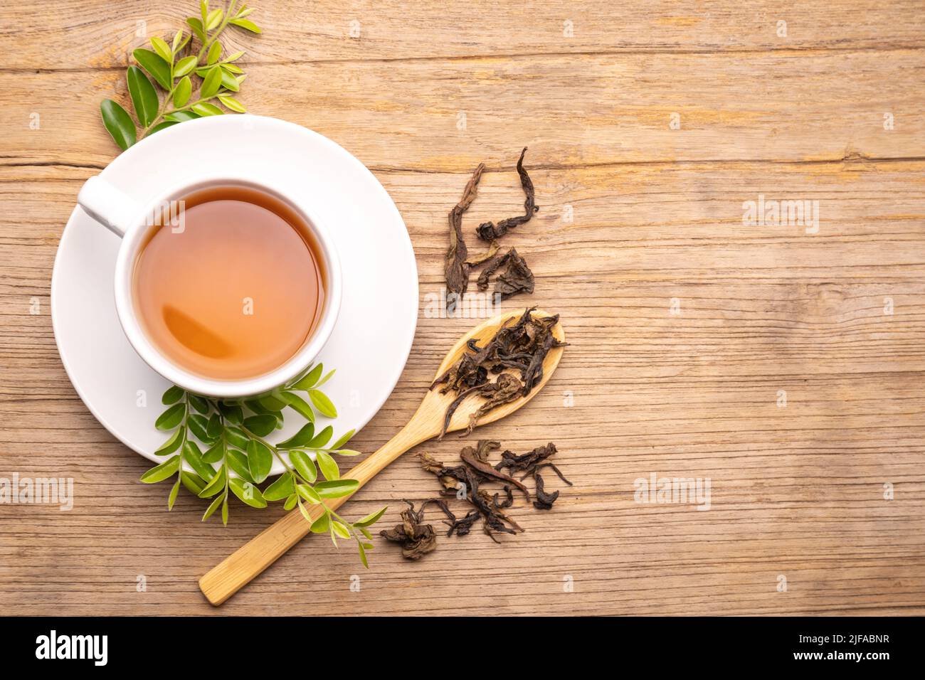 Weiße Tasse heißen Tee und trockenes Teeblatt auf Holztisch Hintergrund Stockfoto