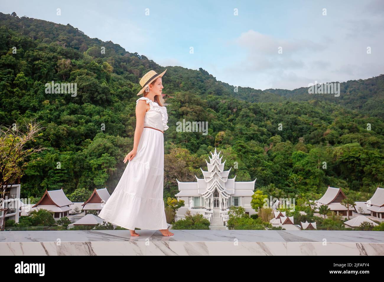 Elegante Reisefrau in Hut und weißem Kleid zu Fuß in Luxus-Resort mit thai-Tempel auf dem Hintergrund. Weibliche Reisende auf Sommer tropischen Ferien auf Stockfoto