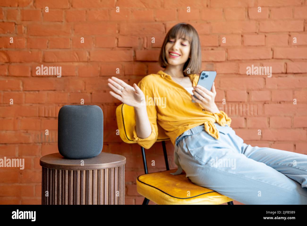 Frau mit Smart-Lautsprecher und Telefon zu Hause Stockfoto