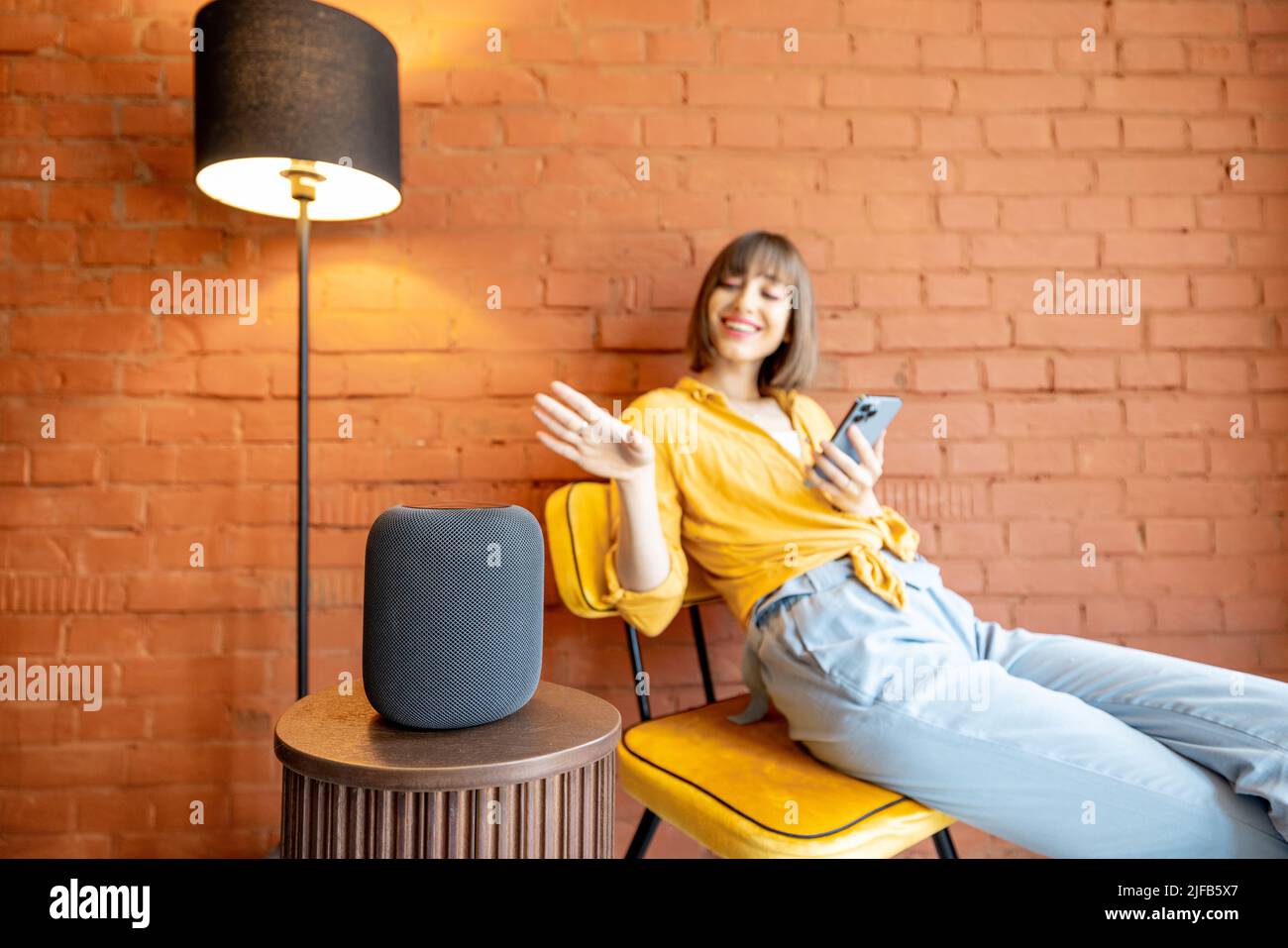 Frau mit Smart-Lautsprecher und Telefon zu Hause Stockfoto