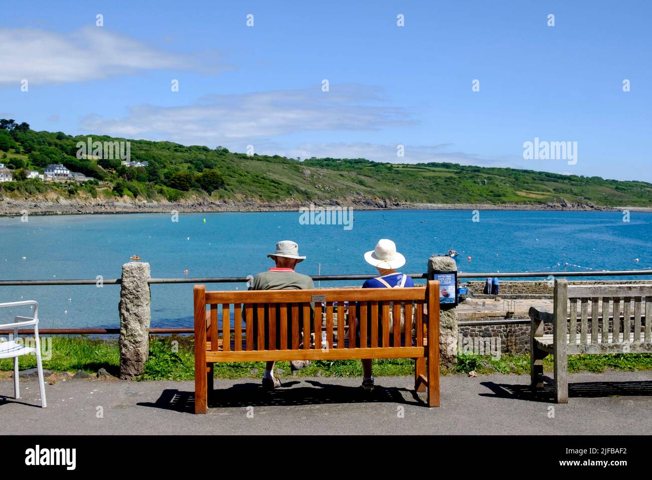 Das ältere Paar saß auf einer Bank mit Blick auf den Hafen von Coverack. Lizard Peninsula Cornwall Großbritannien Stockfoto