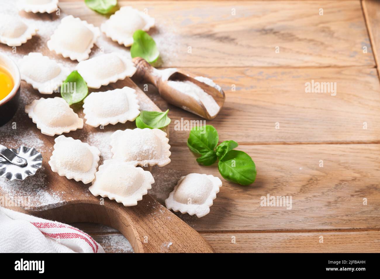 Ravioli, italienische Küche. Leckere hausgemachte Pasta-Ravioli mit Mehl, Tomaten, Eiern und grünem Basilikum auf Holzboden. Prozess der Herstellung italienischer Ravioli Stockfoto