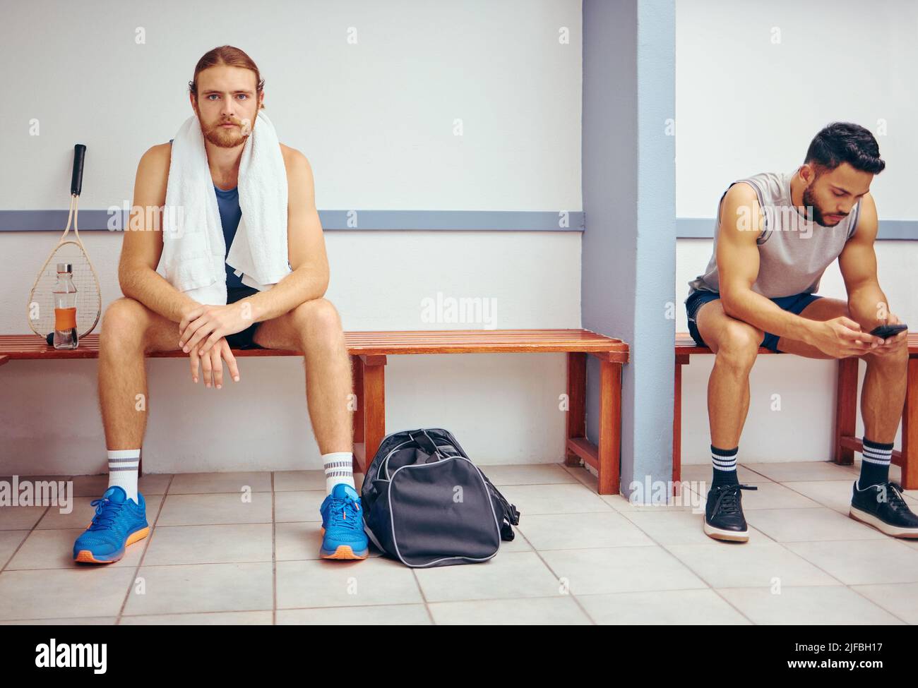 Porträt eines kaukasischen Athleten, der in einer Umkleidekabine sitzt. Zwei Männer sitzen in einem Umkleideraum im Fitnessstudio zusammen. Ernsthafter Spieler, der sich gemeinsam in einem Fitnessstudio entspannt Stockfoto