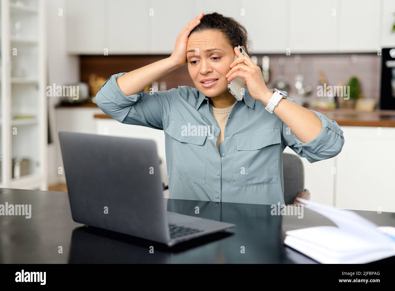 Verärgert und frustriert Frau mit Laptop für Remote-Arbeit von zu Hause aus, nervös über Fehler, stressigen Job, gemischt Rennen Frau sprechen auf dem Smartphone, hat Problem mit der Aufgabe Stockfoto