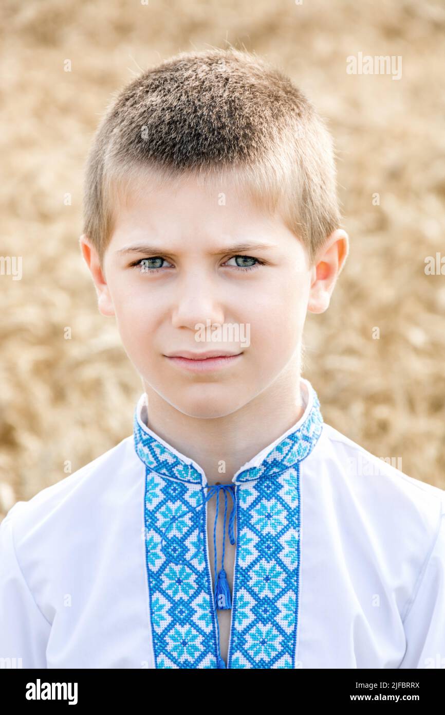 Porträt des Kindes in traditionellen bestickten ukrainischen Hemd auf dem Hintergrund des Weizenfeldes an sonnigen Tag. Blaue Stickerei. Das Gesicht des Jungen ist traurig. Unabhängigkeitstag und die Verfassung der Ukraine Stockfoto