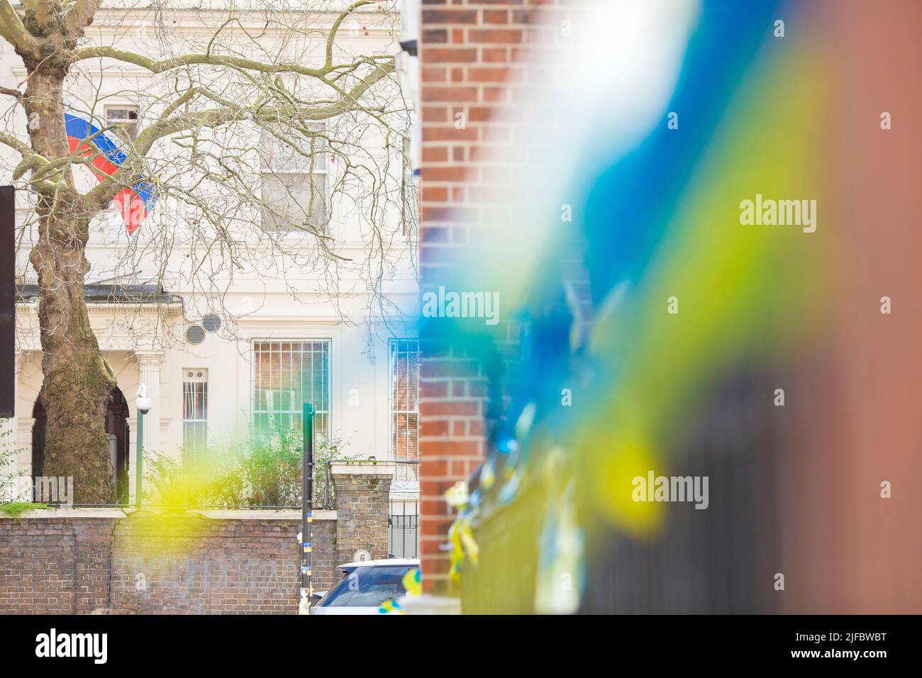 Ukrainische Flaggen, die aus Protest gegen die russische Invasion in der Ukraine gehangen werden, sind in der Nähe der russischen Botschaft zu sehen, wo in London eine russische Flagge fliegt. Stockfoto