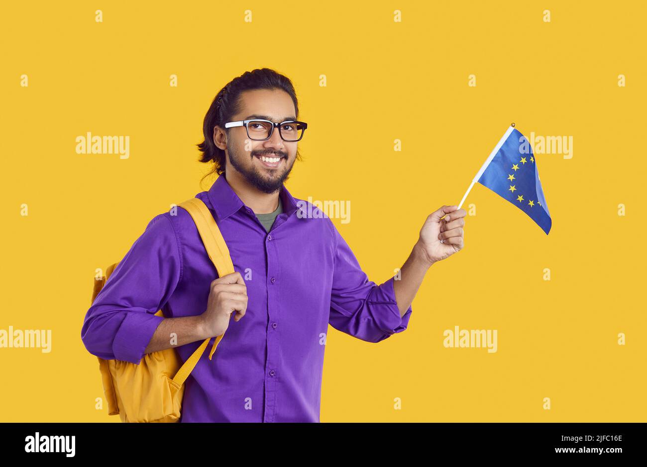 Glücklicher indischer Student isoliert auf gelbem Hintergrund mit Flagge der Europäischen Union und lächelnd Stockfoto