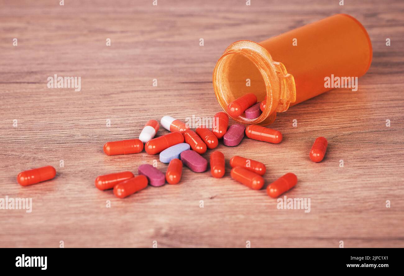 Eine offene orangene Flasche mit bunten Pillen verschüttete sich auf einen Holztisch. Vitaminpräparate sind ein guter Weg, um gesund zu bleiben. Chronische und Stockfoto