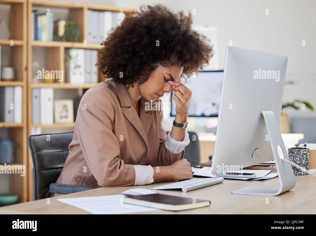 Junge afroamerikanische Geschäftsfrau, die gestresst aussieht, während sie einen Computer an ihrem Schreibtisch im Büro benutzt. Schwarze Frau mit Kopfschmerzen. Frau mit gemischter Rasse Stockfoto