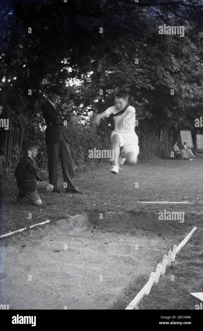 1952, historisch, Schulsport, ein Junge macht den Weitsprung, springt in die Luft in einen Sandkasten, Schottland, Großbritannien. Stockfoto